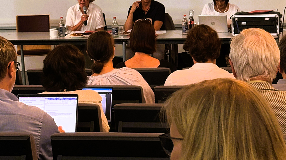 Ein Seminarraum mit Teilnehmern, die auf einem Podium sitzenden Rednern und Laptops.