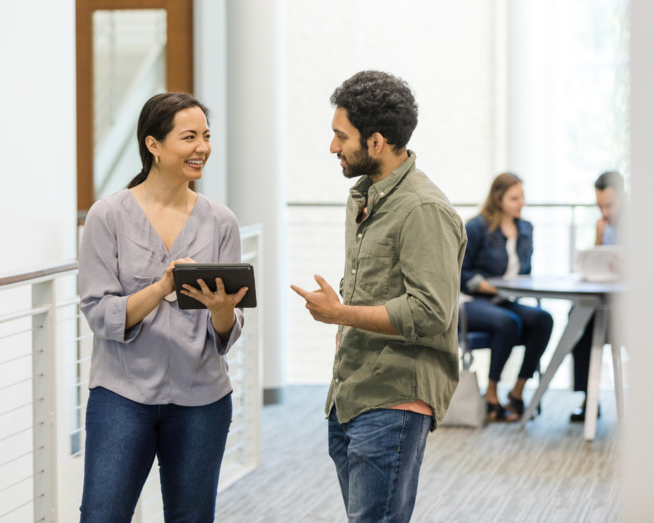 Zwei Personen stehen in einem Büro und unterhalten sich, eine hält ein Tablet.