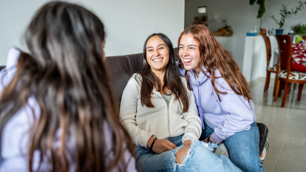 Drei junge Frauen sitzen auf einem Sofa und lachen.