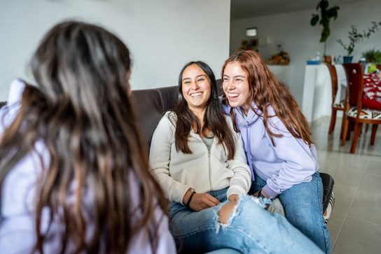 Drei junge Frauen sitzen auf einem Sofa und lachen.