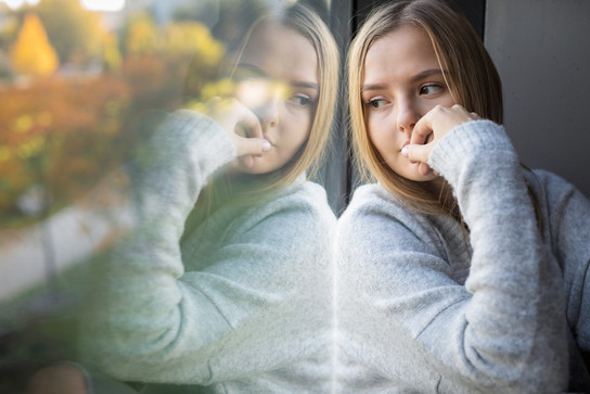Foto: Eine junge Frau sitzt nachdenklich am Fenster